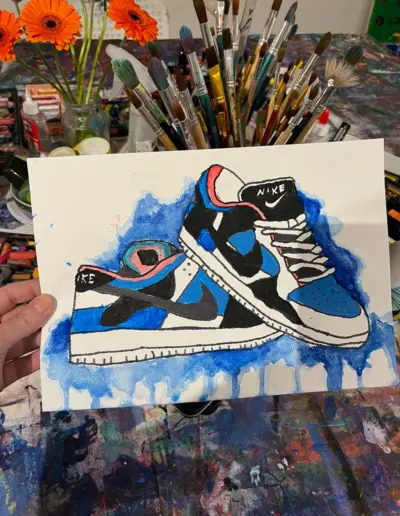 Eine Aquarell-Tusche Zeichnung von blau-weiss-schwarzen Sportschuhen.