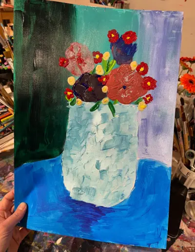 Eine Malerei auf Papier. Das Motiv zeigt bunte Blumen in einer weiss-grauen Vase auf einem blauen Tisch.