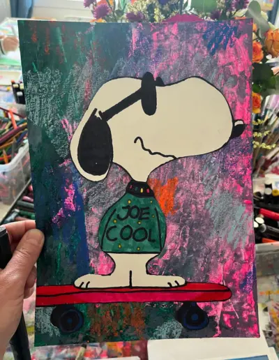 Eine farbenfrohe Zeichnung von der Figur Snoopy mit Sonnenbrille auf einem Skatebooard. Snoopy trägt einen dunkelgrünen Pullover mit der Aufschrift 'Joe Cool'.