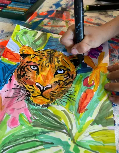 Ein Teilnehmer des Malkurses malt ein Bild von einem Tiger, der von Urwaldpflanzen umgeben ist.