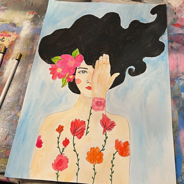 Auf einem Maltisch liegt ein Blatt mit einer Zeichnung von einem Frauenoberkörper mit rotem Blumengesteck in den schwarzen Haaren.