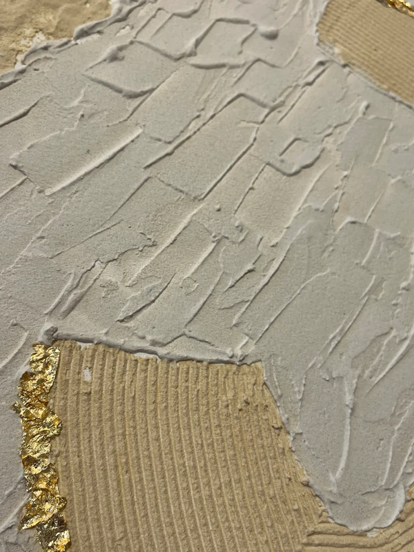 Nahaufnahme von gespachtelter Strukturpaste mit Goldelementen auf Leinwand.