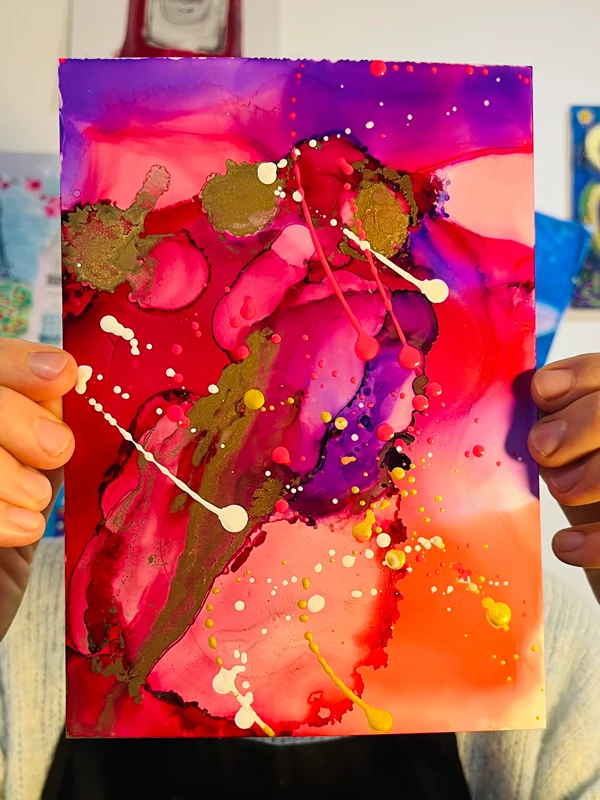 Abstrakte Kunst mit Alkoholtinte in Rot-, Violett-, Goldtönen und Farbspritzern in Weiß, Gold und Pink, entstanden in einem Kreativ-Workshop mit Alkohol & Ink-Technik.