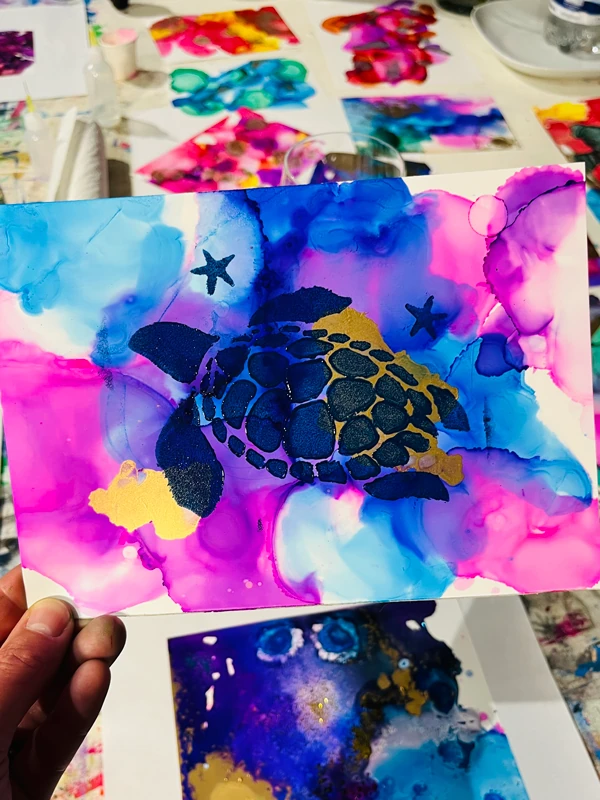 Ein Motiv einer schwimmenden Schildkröte vor abstraktem Hintergrund mit Alkoholtinte in Blau-, Violett- und Goldtönen, entstanden in einem Kreativ-Workshop mit Alkohol & Ink-Technik.