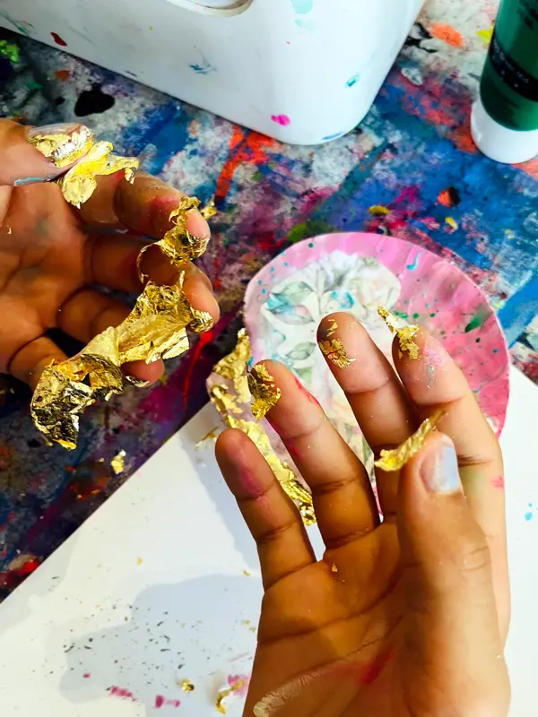 Zwei Hände einer Workshopteilnehmerin mit Blattgold an den Fingern.