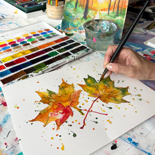 Zwei mit Aquarellfarbe gemalte farbenfrohe Herbstblätter auf weissem Papier.